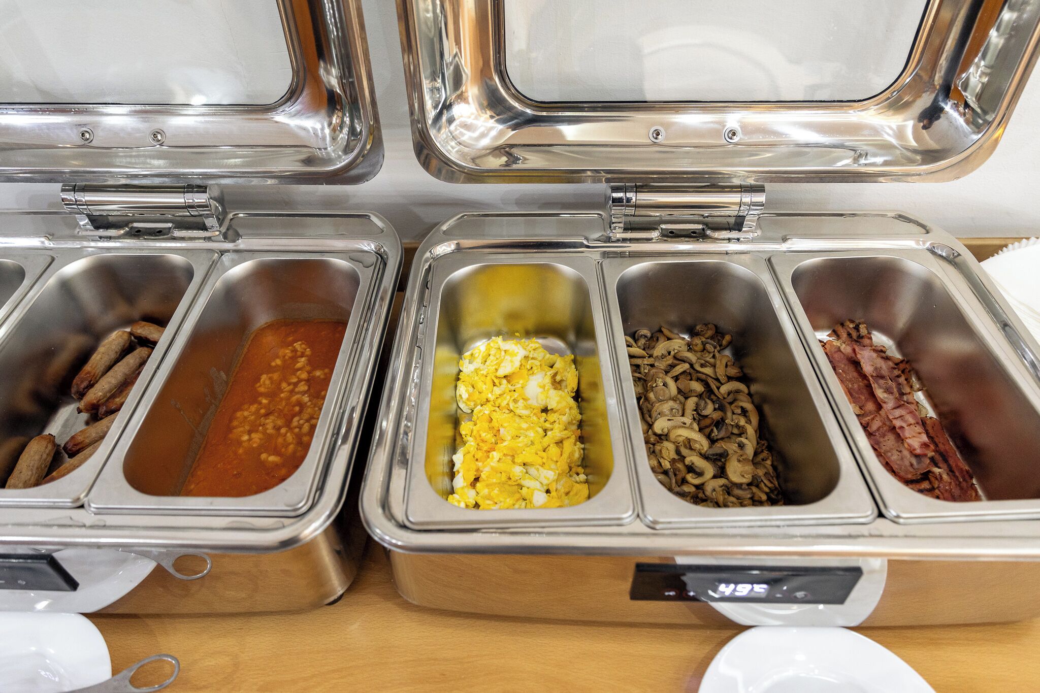 Un buffet proposant une variété de plats, notamment des saucisses, des œufs, des champignons et du bacon.