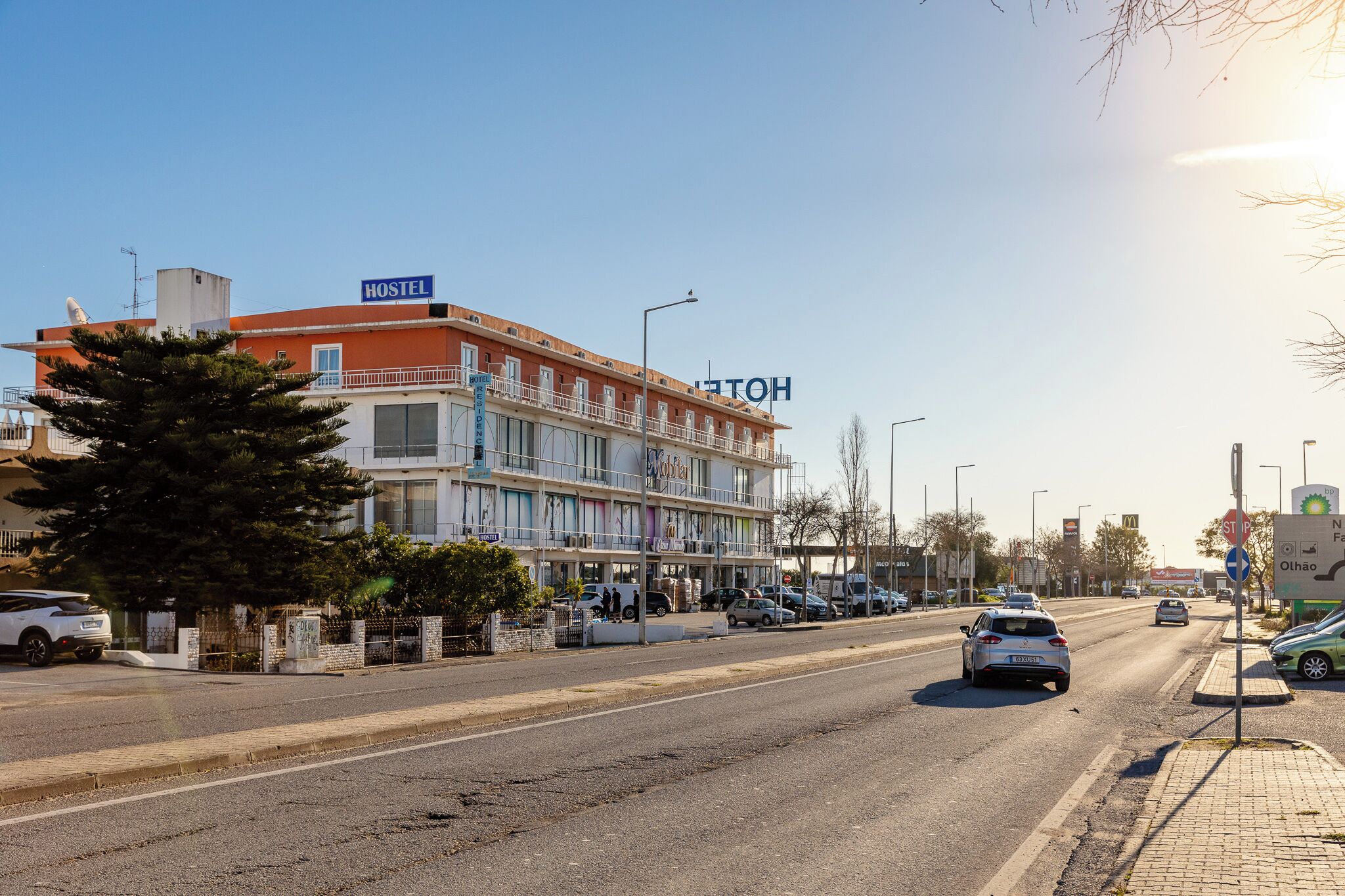A hostel with a signboard, a street with cars, and a clear sky.