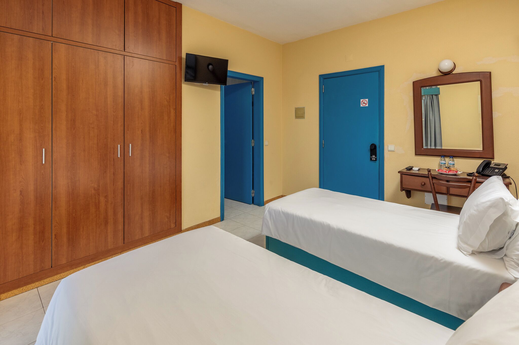 Camera d'albergo con due letti, un armadio in legno, una scrivania con telefono e uno specchio.