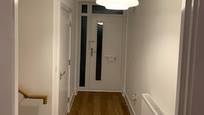 A hallway with a wooden floor, white walls, a white door with a frosted glass panel, and a hanging light fixture. - Brand New Entire 4 Bed House/multiple Parking (South Ockendon)