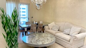 Un salon avec une table ronde en verre, un canapé beige et un lustre.