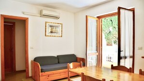 A room with a wooden table and chairs, a sofa, a framed picture on the wall, and a door leading to an outdoor area. - Residence with pool in Alghero  (Alghero)