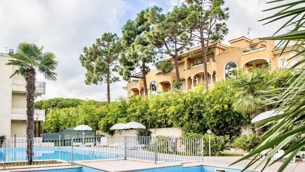 A swimming pool with a tiled deck, surrounded by a fence, and a building with balconies in the background. - Residence with pool in Alghero  (Alghero)