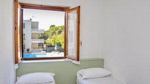 A room with two beds, a window with a view of a swimming pool and buildings, and a green wall. - Residence with pool in Alghero  (Alghero)