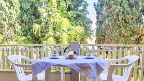 A balcony with a table set for two, surrounded by white plastic chairs, and a view of trees in the background. - Residence with pool in Alghero  (Alghero)