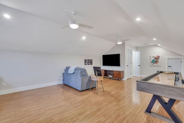 A spacious living room with a ceiling fan, a flat-screen TV, a sofa, a coffee table, and a foosball table.