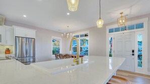 Une cuisine moderne dotée d’un grand îlot central, d’appareils électroménagers en acier inoxydable et offrant une vue sur l’extérieur.