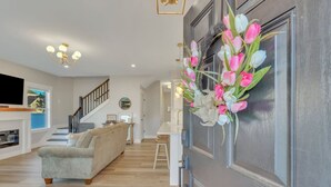 Un salon moderne avec un canapé gris, un plancher en bois, un escalier et une porte agrémentée d’une composition florale.