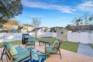 A backyard with a wooden deck, a grill, and outdoor furniture.
