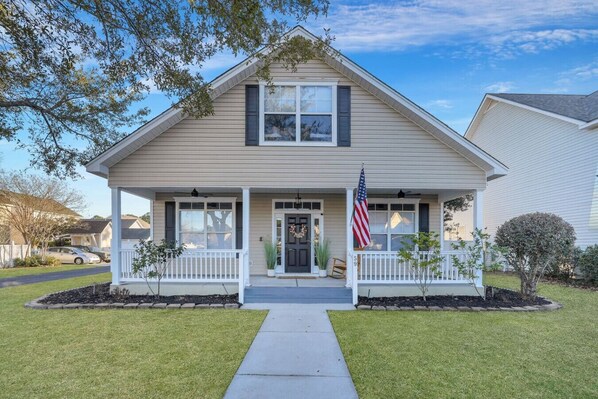 A two-story house with a front porch, a small garden, and an American flag.