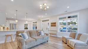 Un grand espace de vie comprenant un canapé, un fauteuil, un tabouret en bois et un coin repas avec un comptoir.