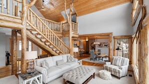Ein großzügiger Wohnbereich mit hoher Holzbalkendecke, einer Treppe, einem Sofa, einem gestreiften Sessel und einem Couchtisch.