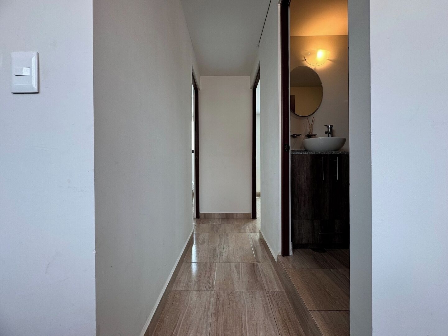 Ein Flur mit Holzboden, der zu einem Badezimmer mit Waschbecken und Spiegel führt.