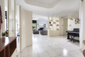 Ein modernes Wohnzimmer mit Klavier, einer Couch und einer Küche im Hintergrund.