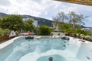 Un bain à remous avec vue sur un paysage montagneux, entouré de plantes en pot et de mobilier d’extérieur.