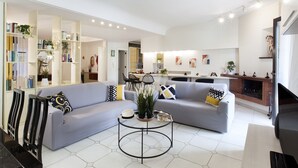 A modern living room with a grey sofa, black and yellow patterned pillows, a coffee table, and a bookshelf filled with books and plants. - Maison Wally in Sorrento (Sorrento)