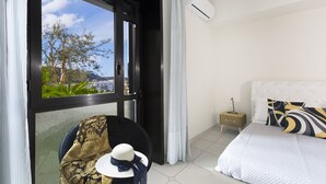 A hotel room with a bed, a chair, a small table, and a window with a view of trees and buildings. - Maison Wally in Sorrento (Sorrento)