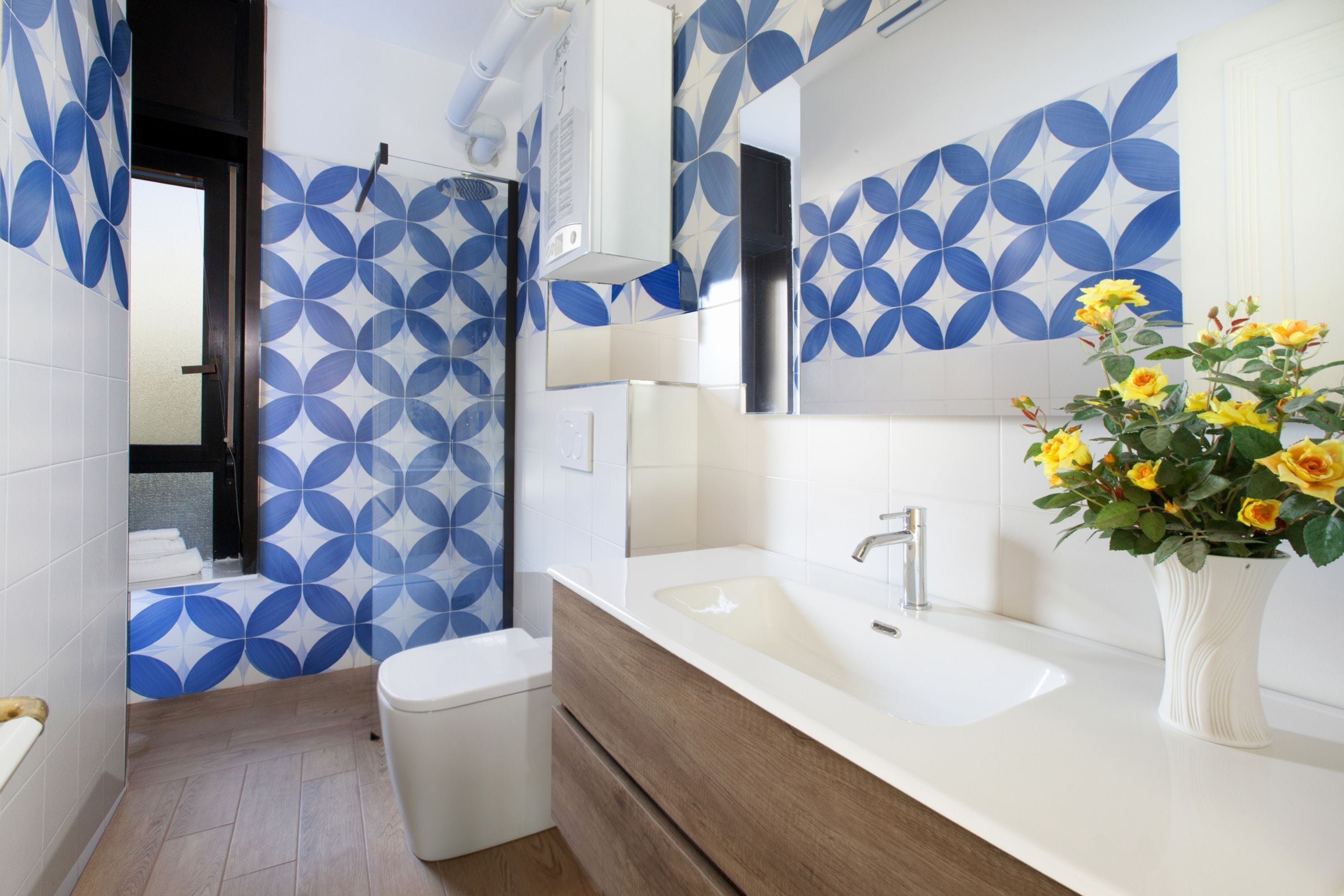 A modern bathroom with a white sink, wooden vanity, and a blue and white patterned wall.