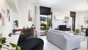 A modern living room with a grey sofa, a black armchair, and a dining area with a table and chairs. There is a large window providing a view of the outdoors. - Maison Wally in Sorrento (Sorrento)