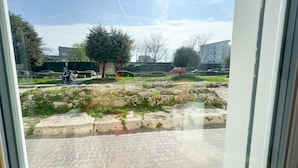 Ein gepflasterter Bereich mit einer Steinmauer und einem Baum in der Mitte, wie er durch ein Fenster zu sehen ist.