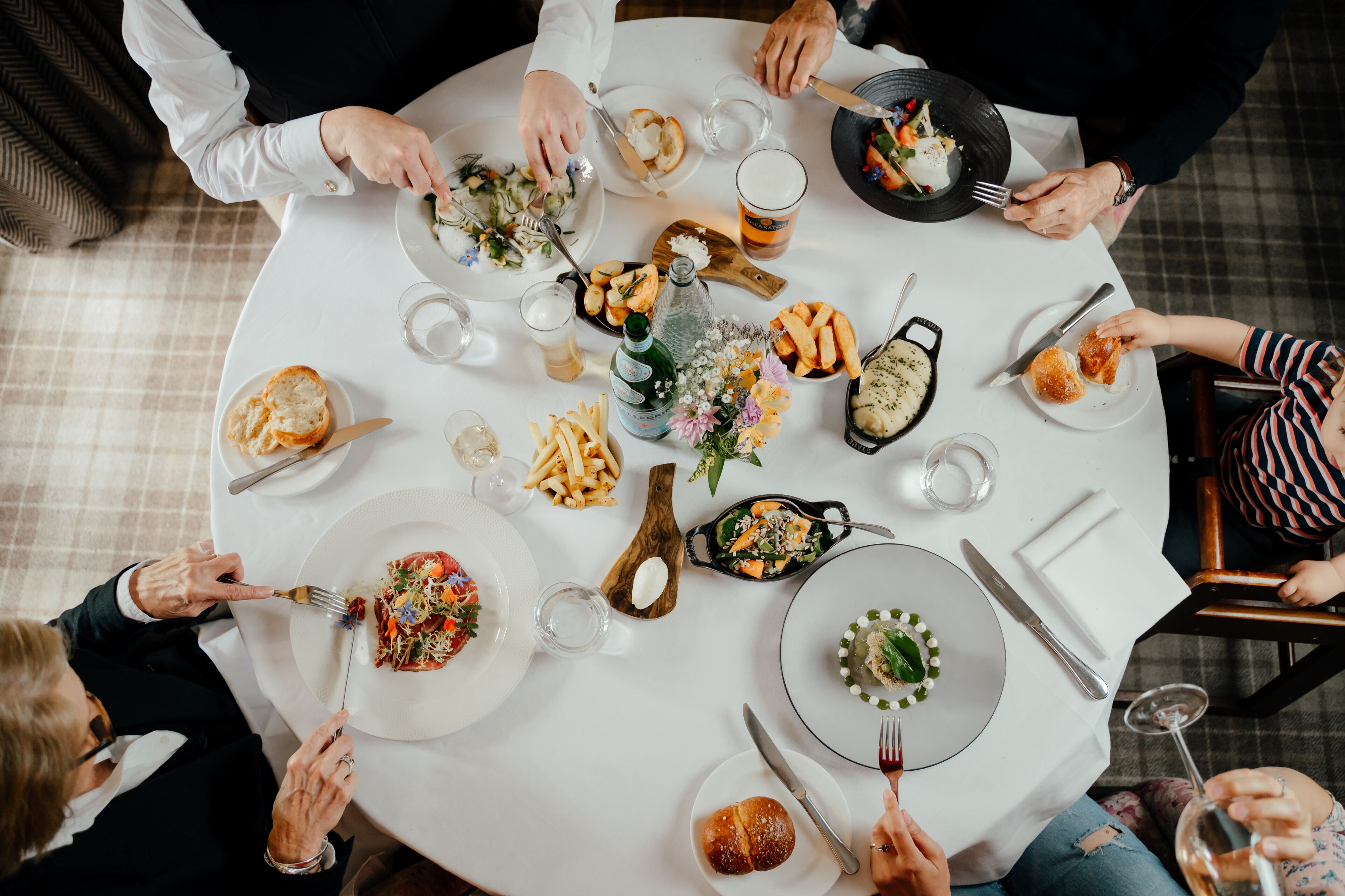 A round table with multiple plates of food, glasses, and cutlery.