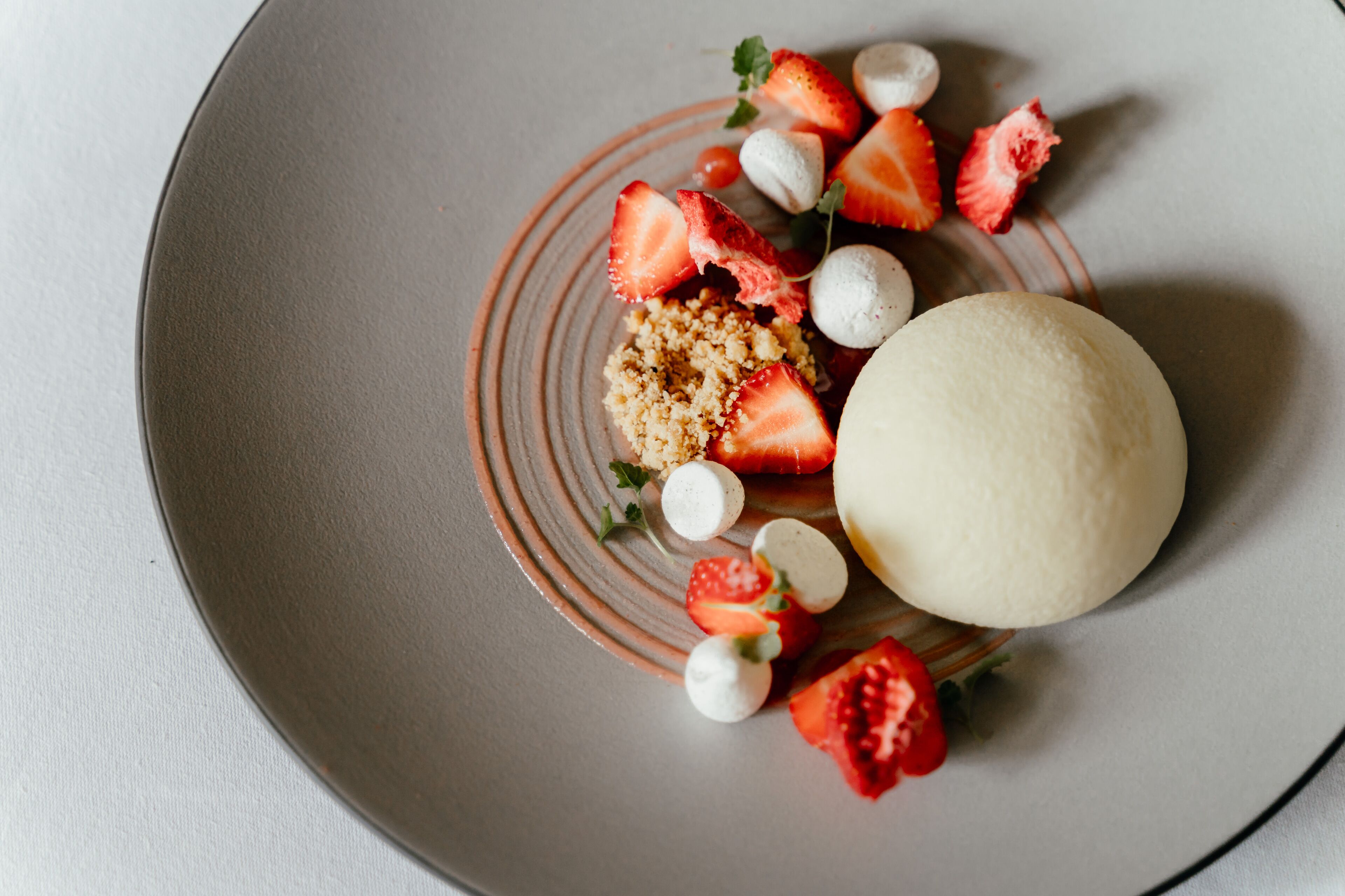 Un piatto dessert con un dolce bianco rotondo, fragole e piccole sfere bianche.
