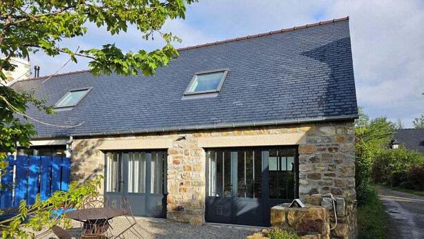 A stone house with a sloped roof, two windows, and a gravel driveway. - 2 Pièces, Jardinet Sud, Calme, 1000 m Morgat (Crozon)