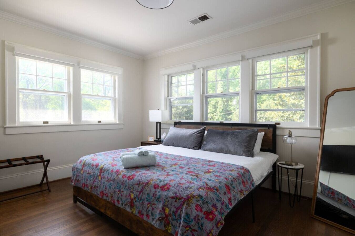 Une chambre à coucher avec un grand lit, de nombreuses fenêtres, une table de chevet avec une lampe et un banc en bois.