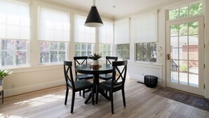 Een eetgedeelte met een ronde tafel, vier stoelen, een hanglamp en grote ramen.