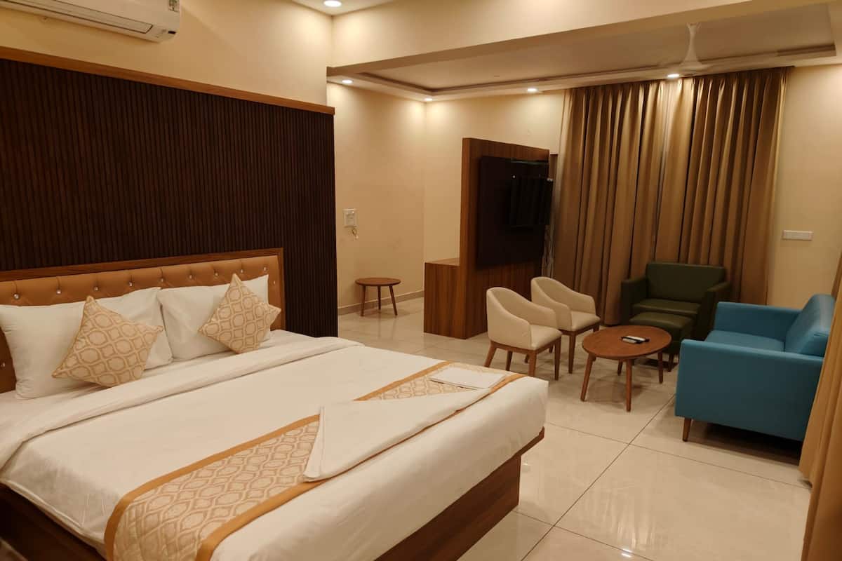 Habitación de hotel con una cama grande, una zona de estar con sillas, una mesita y un televisor.