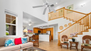 A spacious living area with a sofa, coffee table, and wicker chairs. A kitchen is visible in the background, and a wooden staircase leads to an upper level. - *FREE LATE CHECK OUT Jun 1-Sep 30/2201 Waikoloa Colony Villas (Waikoloa Beach Resort)