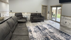 Un salón amplio con un sofá seccional grande, un sofá más pequeño y una mesa de centro. Una ventana grande ofrece luz natural y vistas al exterior.