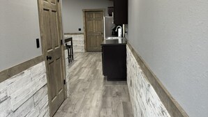 Un pasillo estrecho con suelo de madera, un banco de color oscuro y una zona de lavamanos con espejo.
