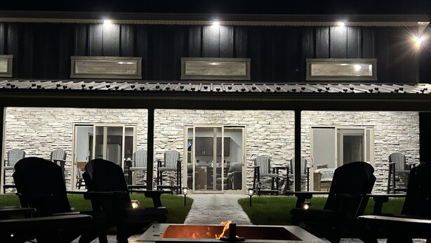 Un patio al aire libre con muros de piedra, un hogar para fuego y varias sillas Adirondack.