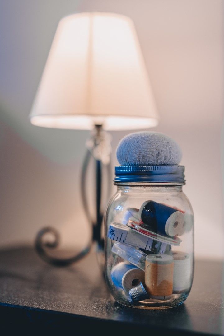 Ein Glas mit Deckel, gefüllt mit aufgerollten Gegenständen, steht auf einer Oberfläche. Im Hintergrund steht eine Lampe.