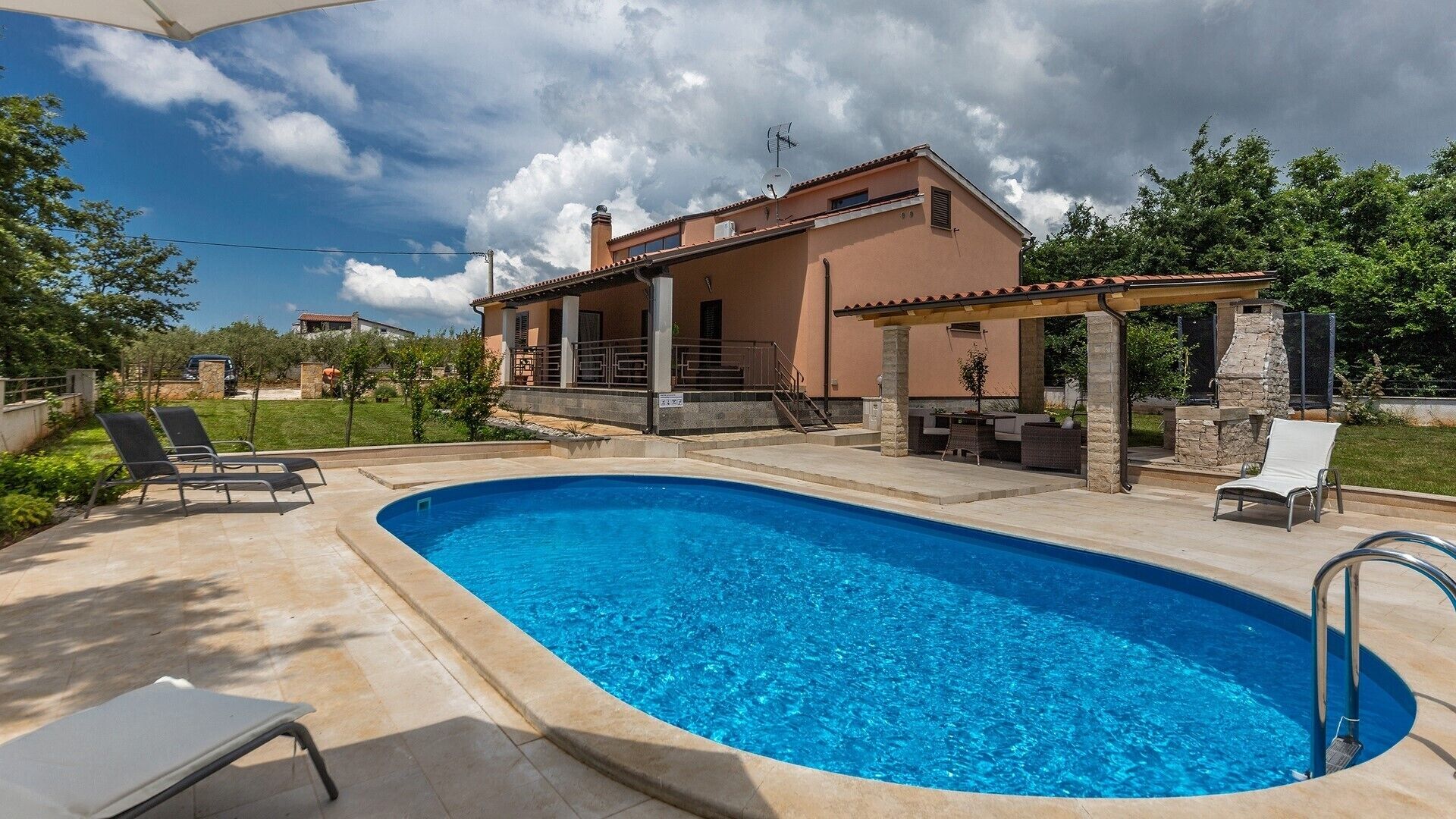 Ein Swimmingpool mit Liegestühlen, eine überdachte Terrasse und ein Haus mit Steinverkleidung.