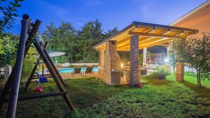 Ein Garten mit Grillplatz aus Stein, einer Schaukel und einem Pool.