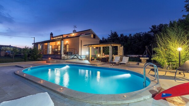 Ein modernes Haus mit Schwimmbad, Sitzgelegenheiten im Freien und einer gut beleuchteten Terrasse.