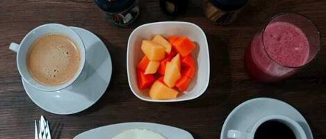 Desayuno con tostadas, huevos, café, un batido y condimentos sobre una mesa de madera.