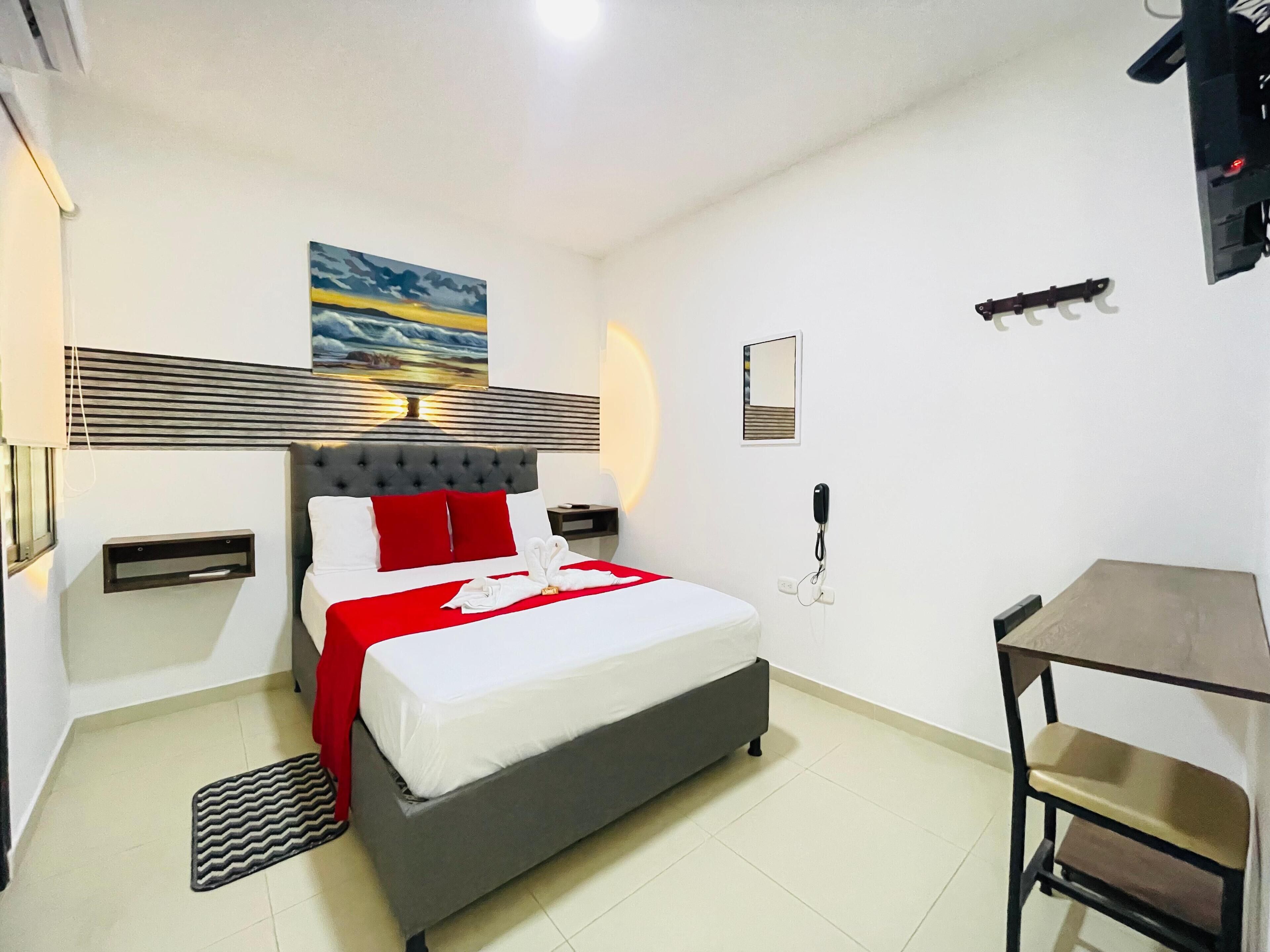 Habitación de hotel con cama, mesitas de noche, escritorio, silla, teléfono y un cuadro en la pared.