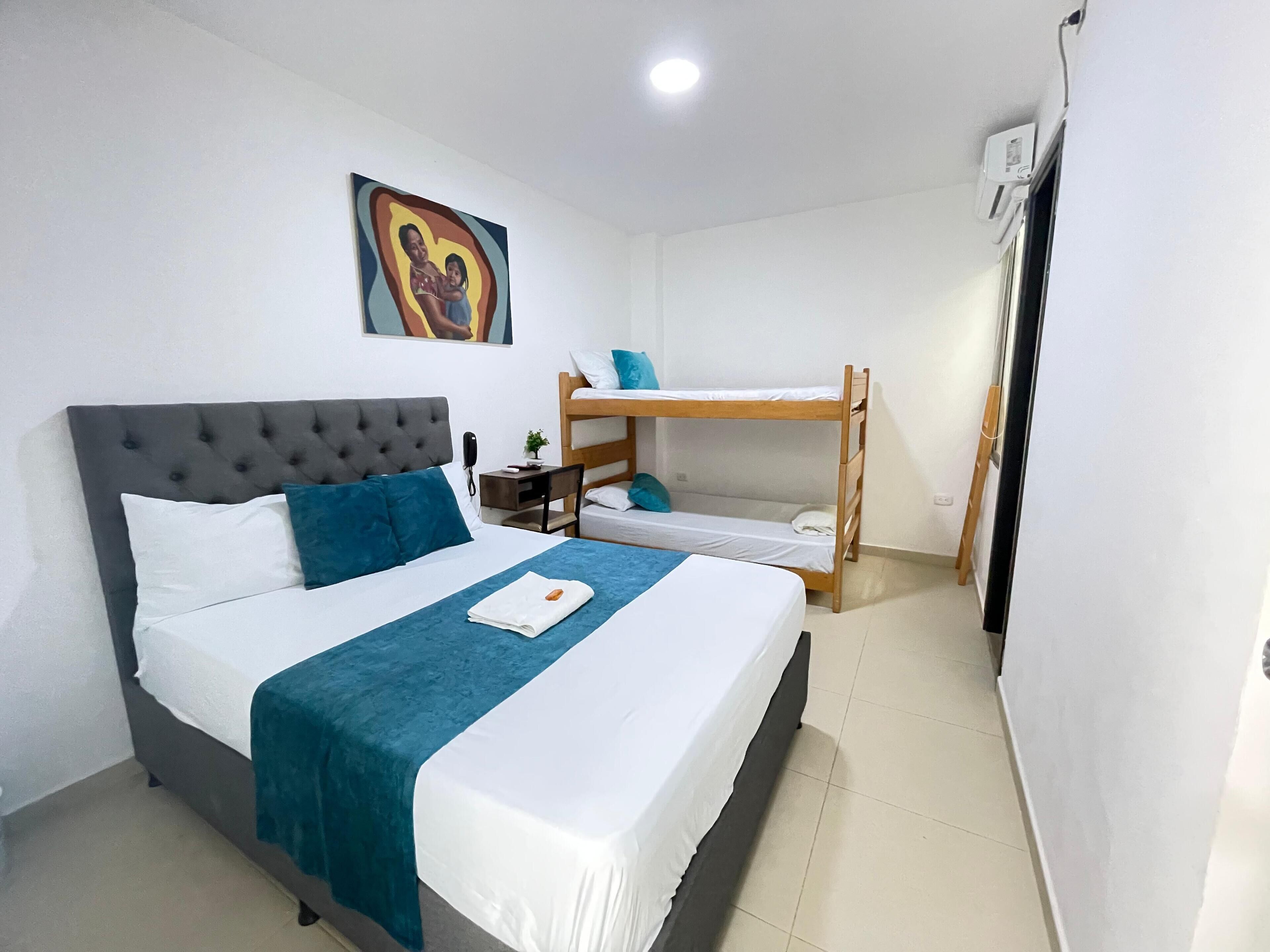 A bedroom with a large bed, a smaller bunk bed, a bedside table, a phone, and a painting on the wall.