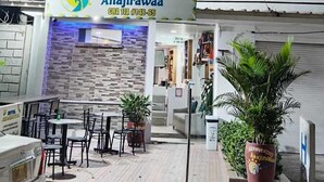Ett hotell som heter ”Anajirawaa” med en modern fasad, en uteservering och tydlig skyltning.