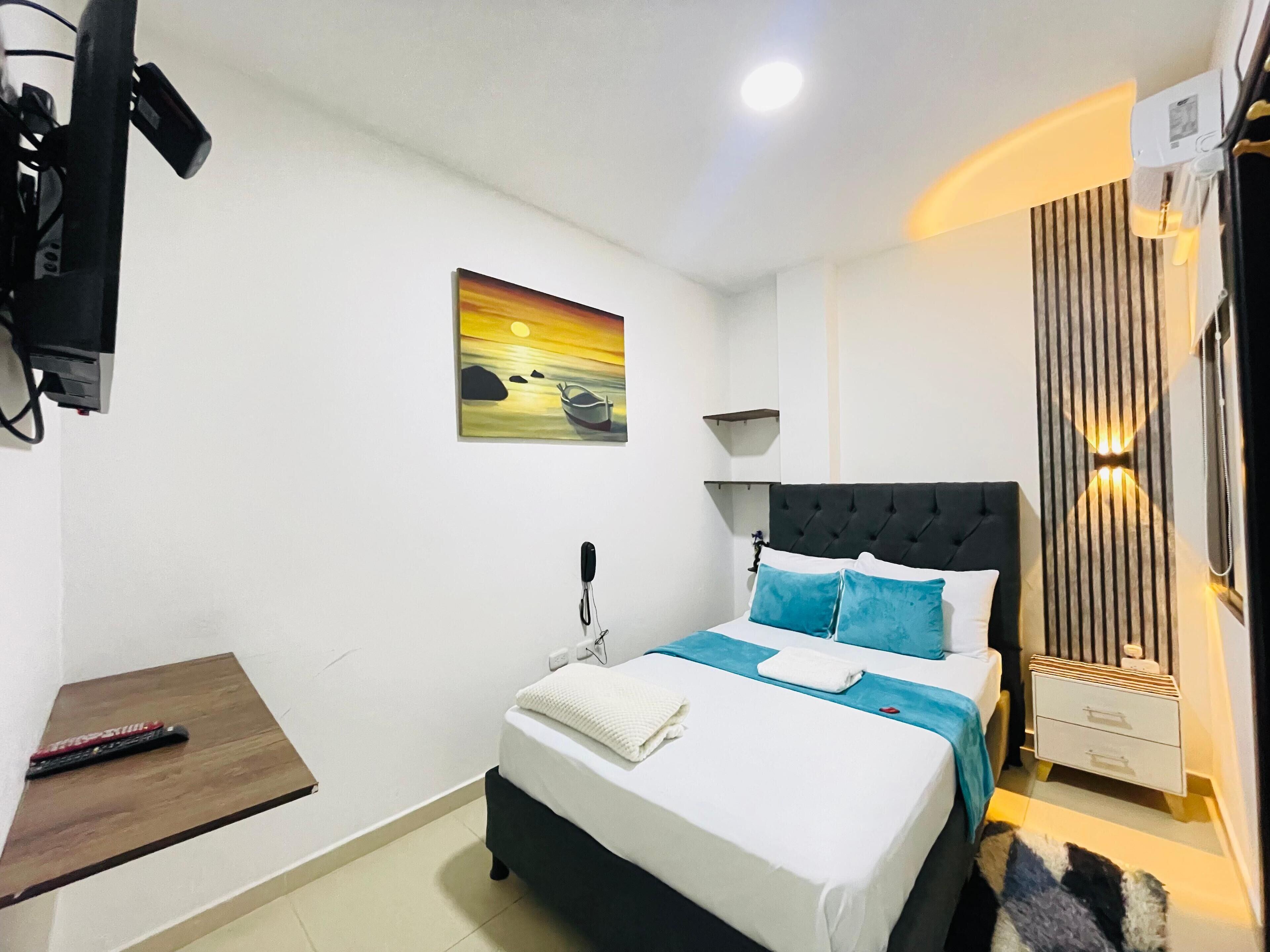 A bedroom with a bed, bedside table, and a painting on the wall.