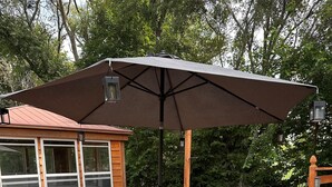 A wooden deck with a glass table and chairs, an umbrella, and a wooden cabin with windows. - Quiet Getaway 5 minutes from Galesburg with pool and hot tub (Galesburg)