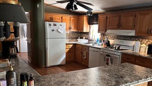 A kitchen with wooden cabinets, a granite countertop, a refrigerator, a stove, and a ceiling fan. - Quiet Getaway 5 minutes from Galesburg with pool and hot tub (Galesburg)