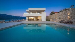 Une maison moderne à deux étages, dotée d’une piscine, d’un espace salon extérieur et d’un mur en pierre.