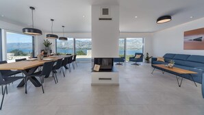Un salon moderne doté d’une grande cheminée, d’un coin repas offrant une vue sur la mer et d’un canapé bleu.