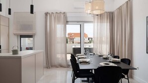 Een moderne eetruimte met een lange tafel voor zes personen, zwarte stoelen en uitzicht op een stadsgezicht door grote ramen.