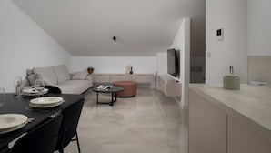 A modern, minimalist living space with a dining area, sofa, and a television mounted on the wall.