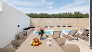 A poolside area with a table set for two, a vase with flowers, and lounge chairs.